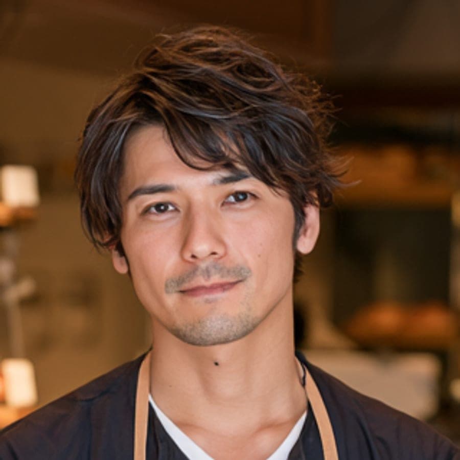 紺のシャツにベージュのエプロンをつけた作り手の顔。背景はぼけた売り場